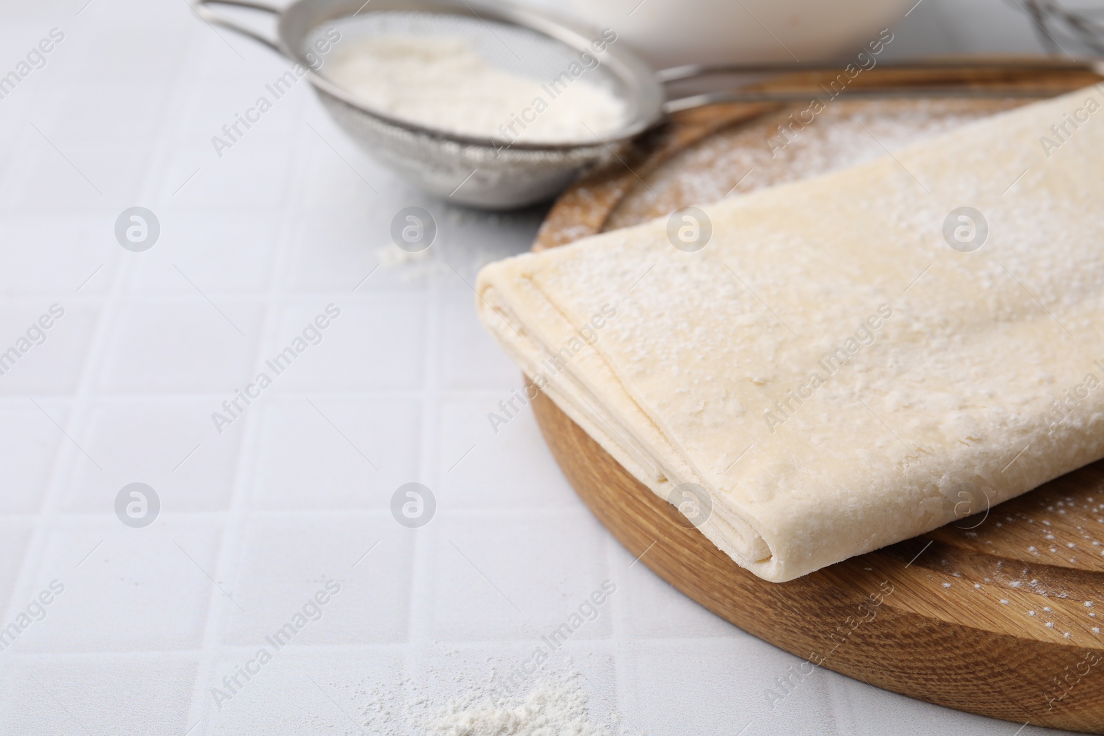 Photo of Raw puff pastry dough on white tiled table, closeup. Space for text