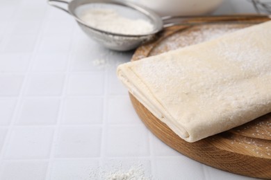 Raw puff pastry dough on white tiled table, closeup. Space for text