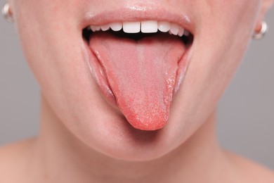 Woman showing her tongue on grey background, closeup
