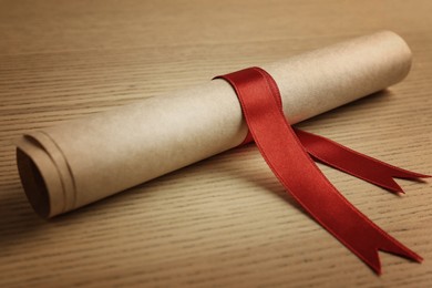 Image of Graduation diploma tied with red ribbon on wooden table, closeup