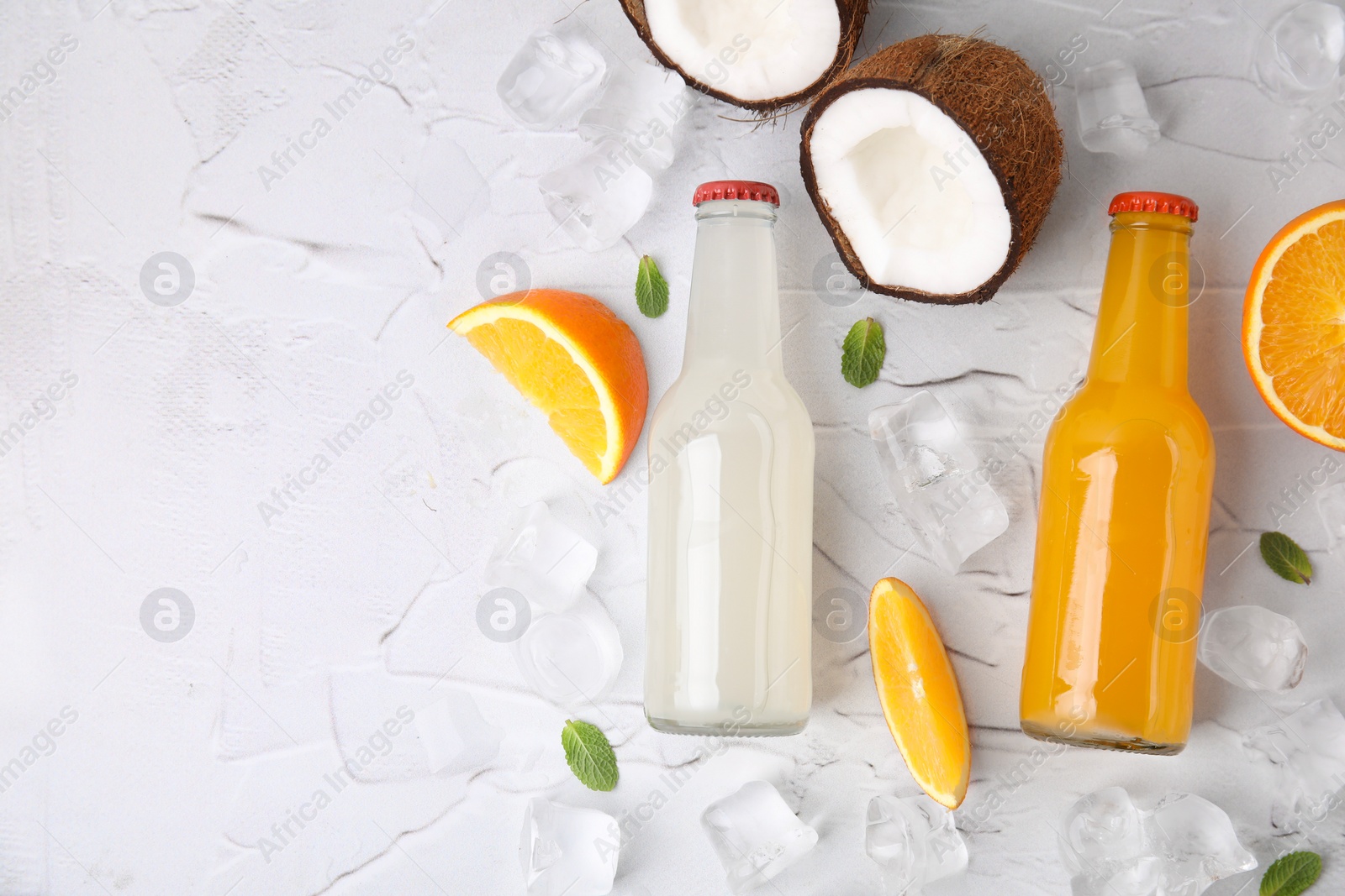 Photo of Tasty kombucha in glass bottles, fresh fruits and ice on white textured table, flat lay. Space for text