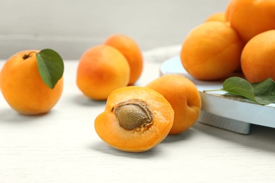 Photo of Delicious ripe sweet apricots and board on white wooden table, closeup view