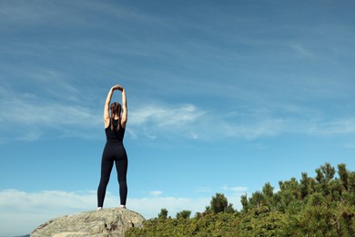 Photo of Beautiful young woman stretching on rock in mountains, back view