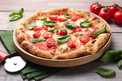 Photo of Delicious Margherita pizza and cutter on wooden table, closeup
