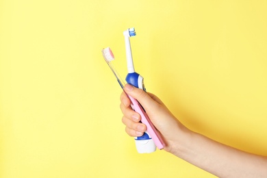 Photo of Woman holding manual and electric toothbrushes against color background