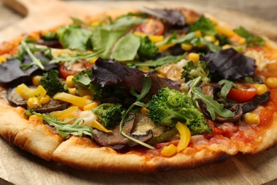 Photo of Delicious vegetarian pizza with mushrooms, vegetables and greens on wooden board, closeup