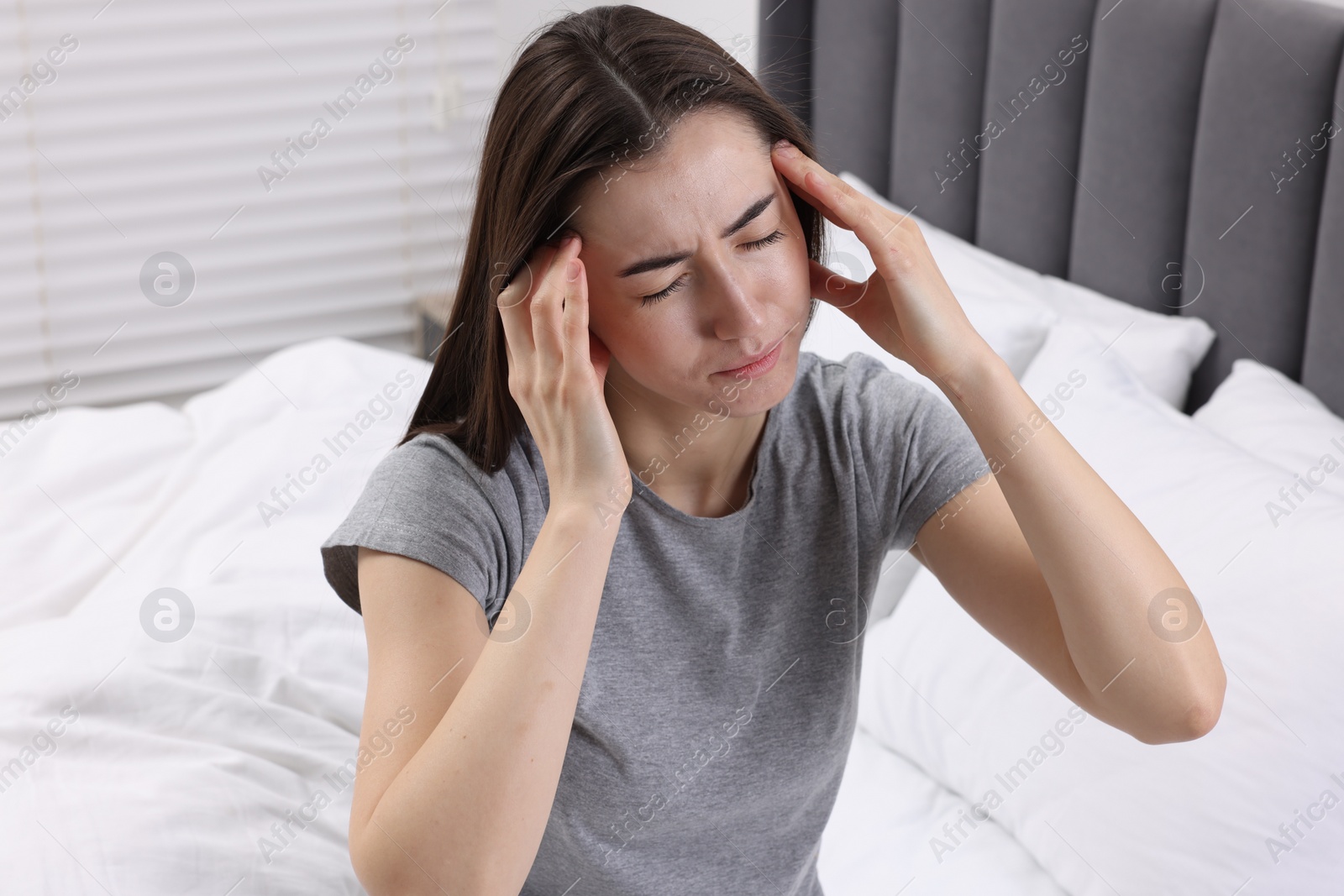 Photo of Sad woman suffering from headache on bed indoors