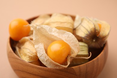 Ripe physalis fruits with calyxes in bowl on beige background, closeup