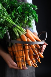 Woman holding basket with ripe carrots on black background, closeup