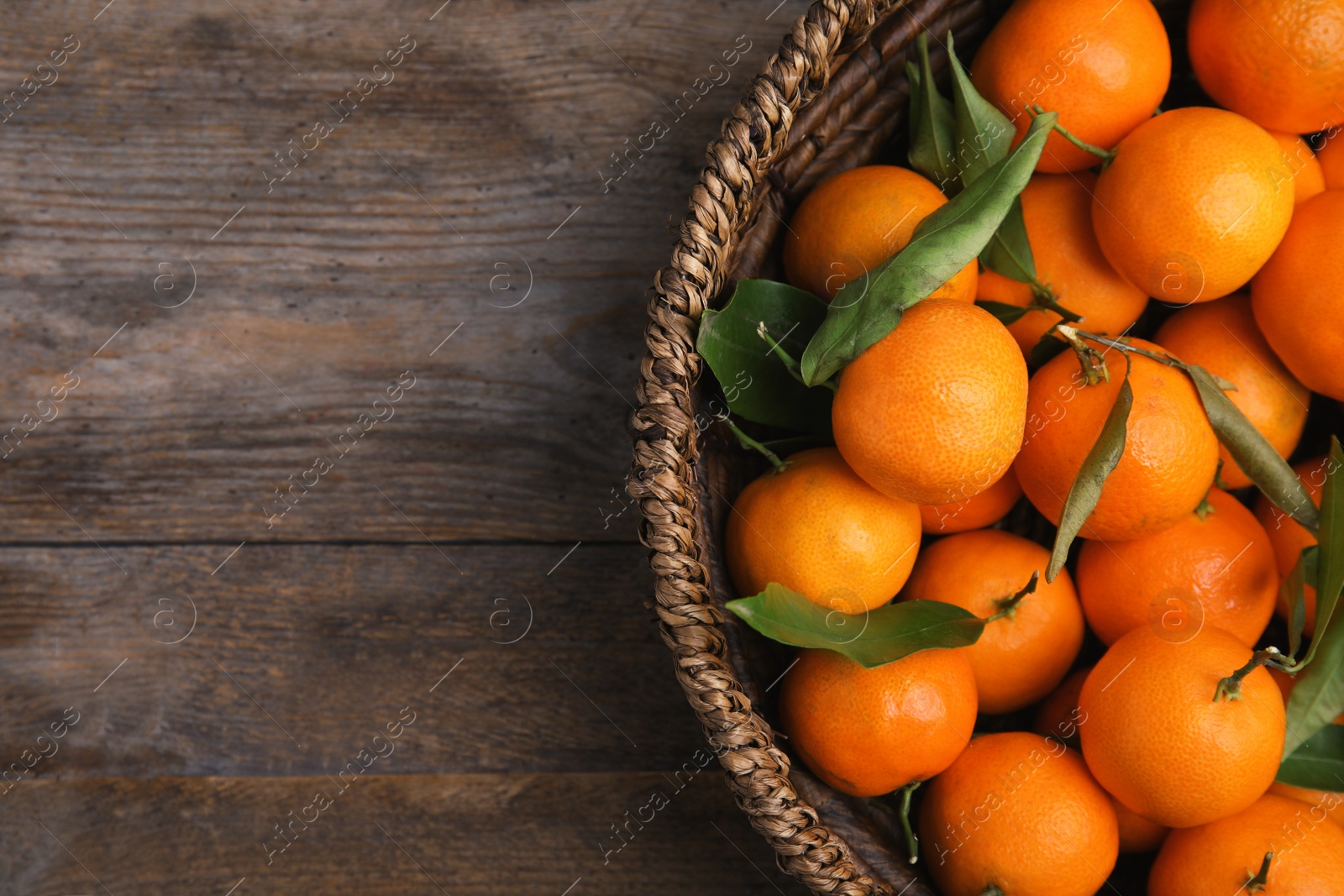 Photo of Fresh ripe tangerines in wicker basket and space for text on wooden background, top view