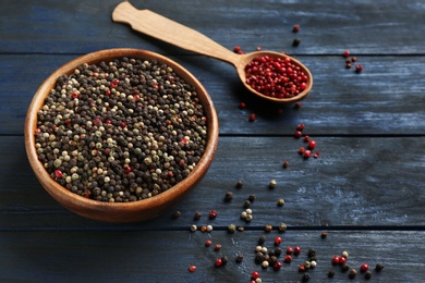 Photo of Mix of peppercorns in bowl on dark wooden table, above view