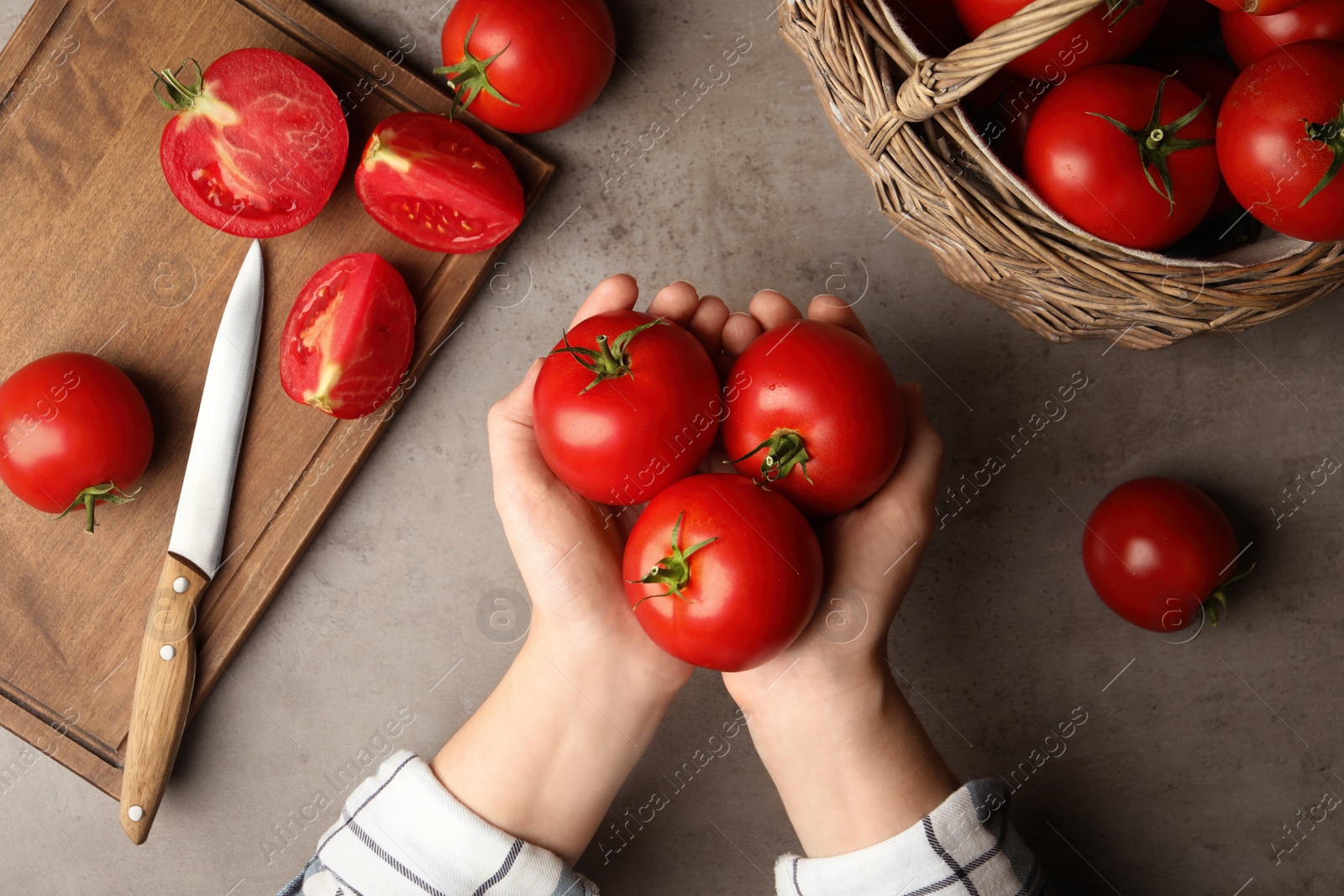 Photo of Woman with ripe tomatoes at grey table, top view