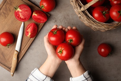 Woman with ripe tomatoes at grey table, top view