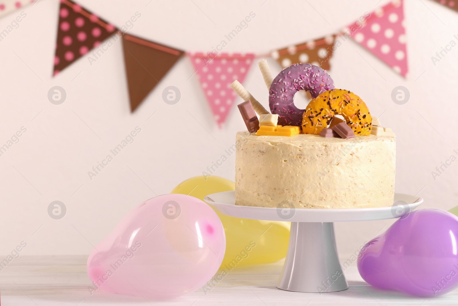 Photo of Delicious cake decorated with sweets and balloons on white wooden table, space for text