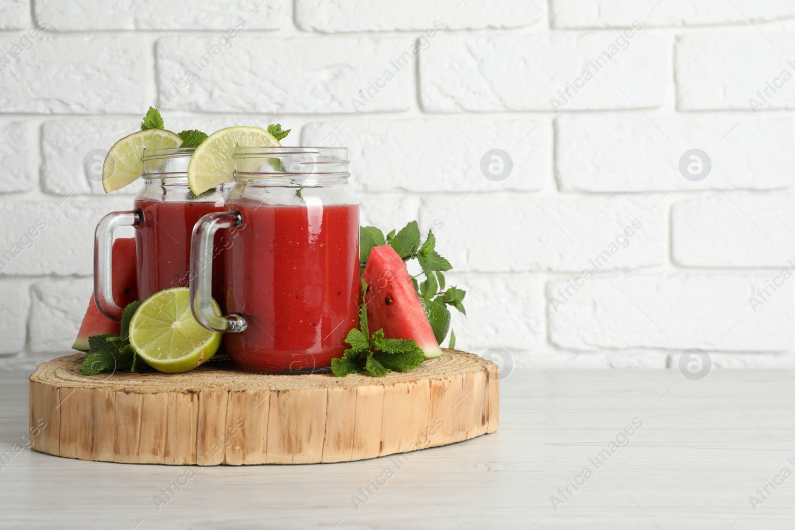 Photo of Tasty summer watermelon drink, limes and mint on white wooden table, space for text