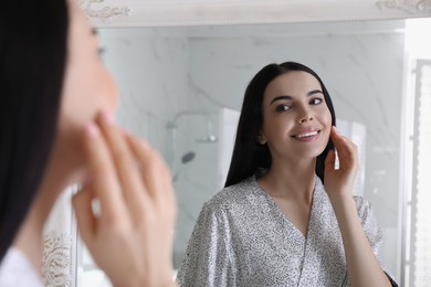 Photo of Beautiful young woman looking at herself in bathroom mirror