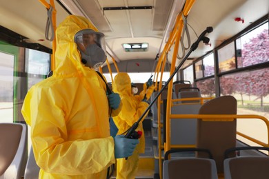 Photo of Public transport sanitation. Workers in protective suits disinfecting bus salon