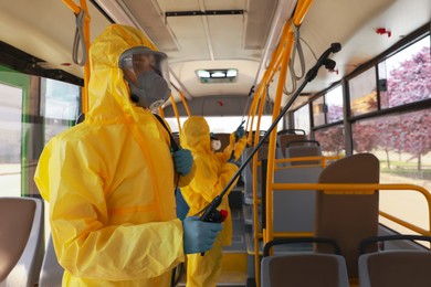 Public transport sanitation. Workers in protective suits disinfecting bus salon