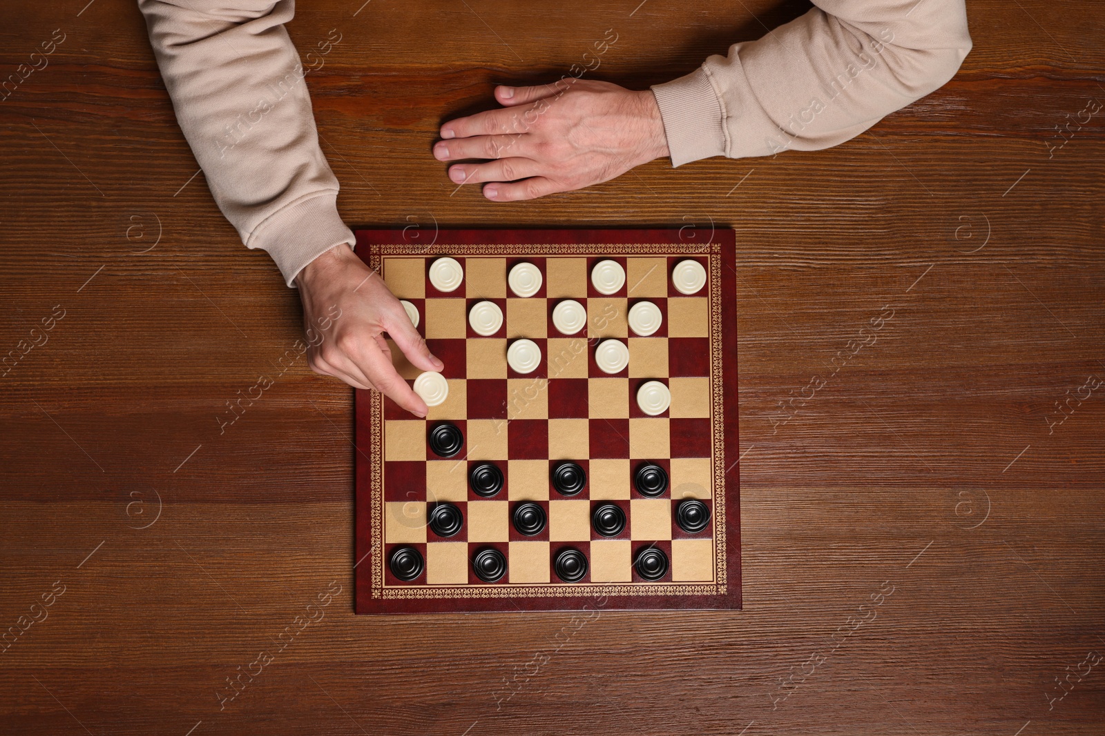 Photo of Playing checkers. Man thinking about next move at wooden table, top view