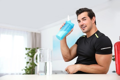 Photo of Young athletic man with protein shake at home, space for text