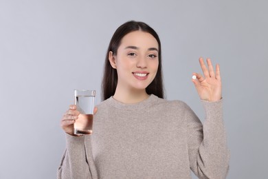 Photo of Happy woman with glass of water showing pill on gray background