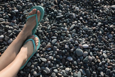 Photo of Woman in stylish flip flops on pebble beach, closeup. Space for text