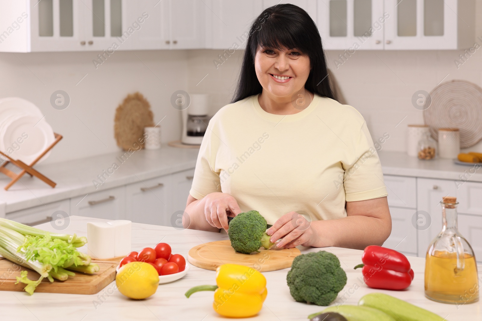 Photo of Beautiful overweight woman preparing healthy meal at table in kitchen