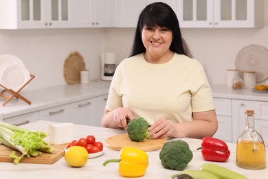 Beautiful overweight woman preparing healthy meal at table in kitchen