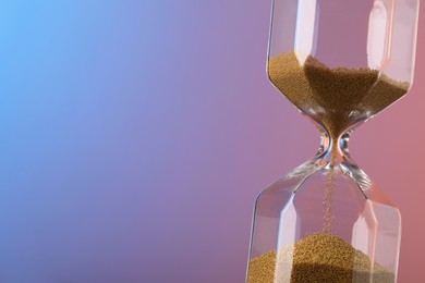 Photo of Hourglass with flowing sand on color background. Space for text