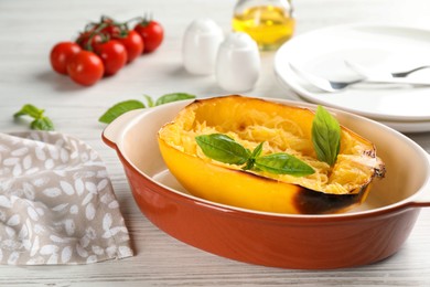Photo of Half of cooked spaghetti squash with basil in baking dish on white wooden table