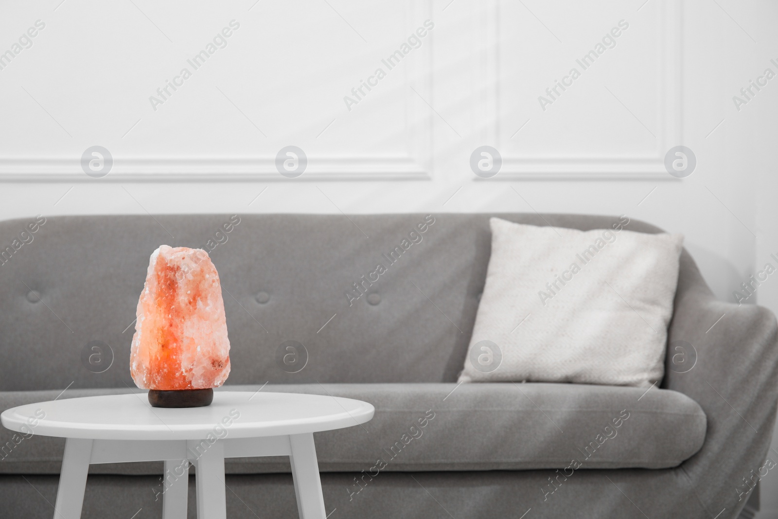 Photo of Himalayan salt lamp on table near sofa in room. Space for text