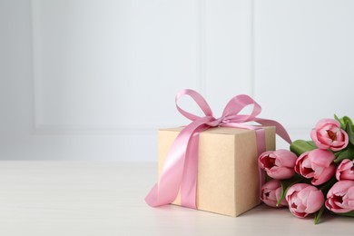 Beautiful gift box with bow and pink tulip flowers on white wooden table, space for text