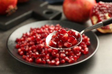 Photo of Eating ripe juicy pomegranate grains at grey table, closeup