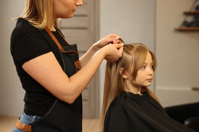 Photo of Professional hairdresser braiding girl's hair in beauty salon