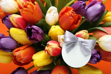 Photo of Bouquet of beautiful colorful tulips with blank card on orange background, closeup. Birthday celebration