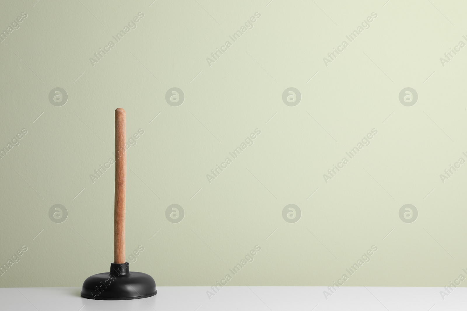 Photo of Plunger on white table against light background. Space for text