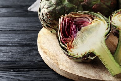 Cut and whole fresh raw artichokes on black wooden table, closeup. Space for text