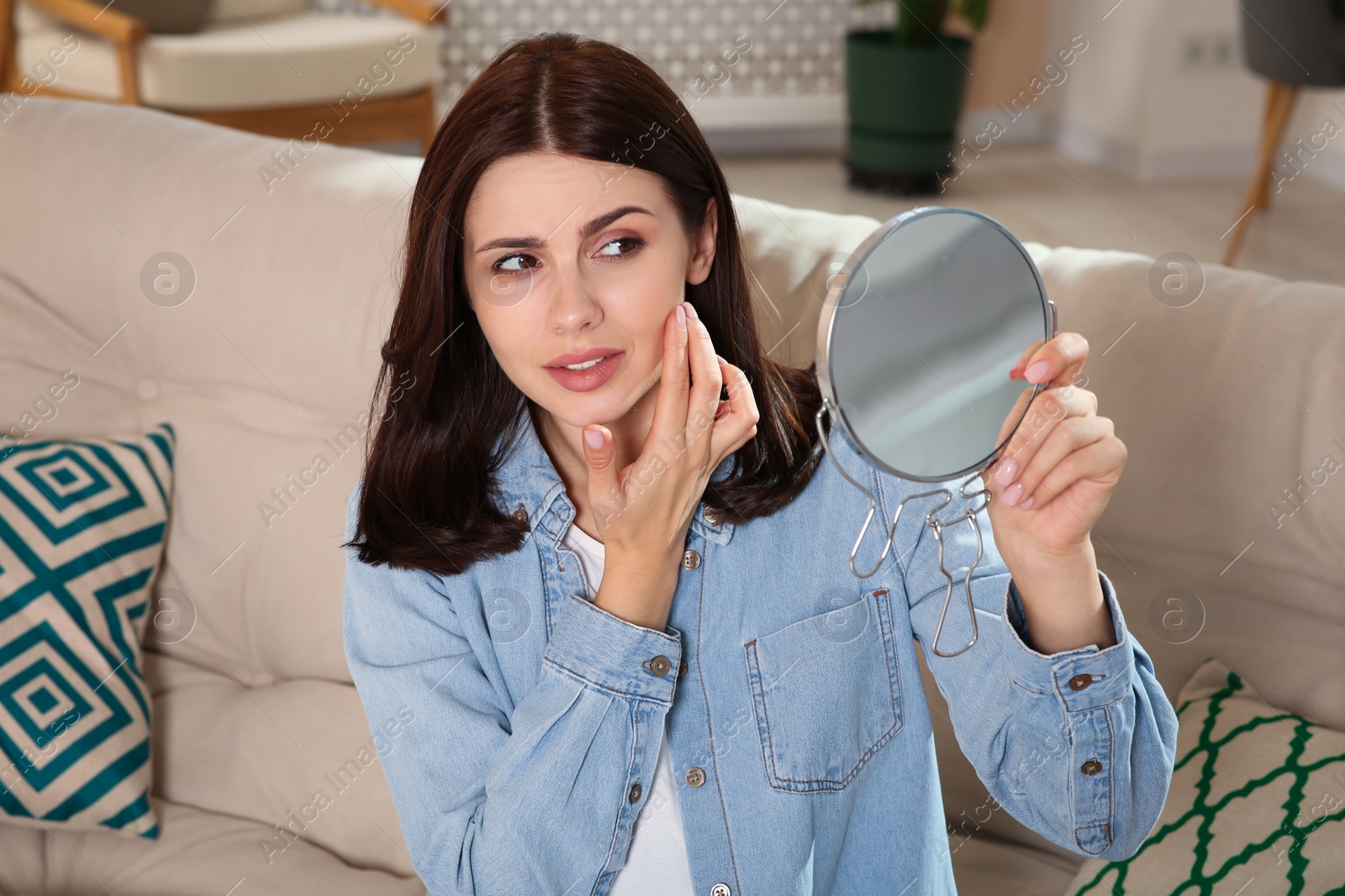 Photo of Young woman looking in mirror and squeezing pimple indoors. Hormonal disorders