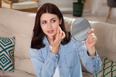 Photo of Young woman looking in mirror and squeezing pimple indoors. Hormonal disorders