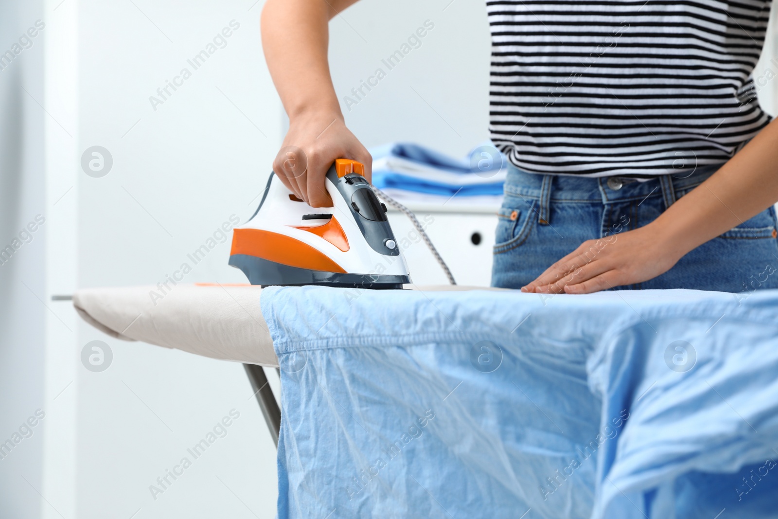 Photo of Young woman ironing clothes on board at home, closeup