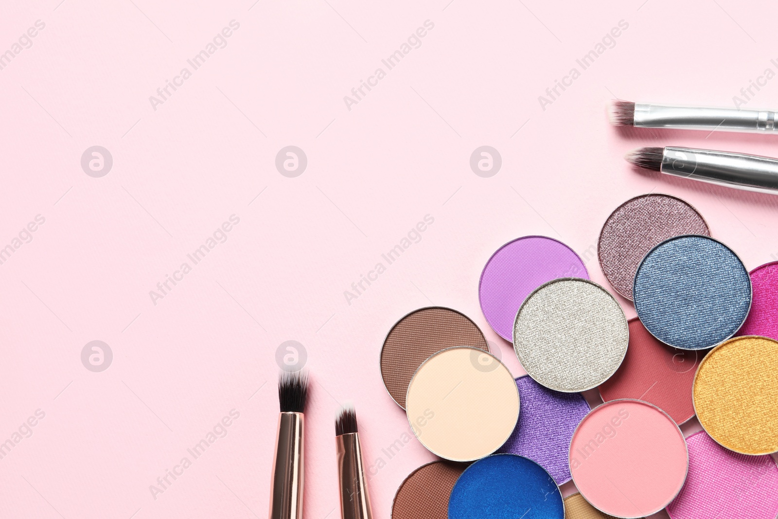 Photo of Different beautiful eye shadows and makeup brushes on pink background, flat lay. Space for text