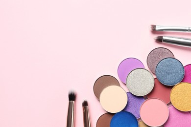 Photo of Different beautiful eye shadows and makeup brushes on pink background, flat lay. Space for text