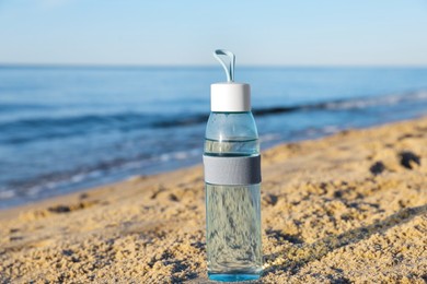Photo of Glass bottle with water on wet sand near sea