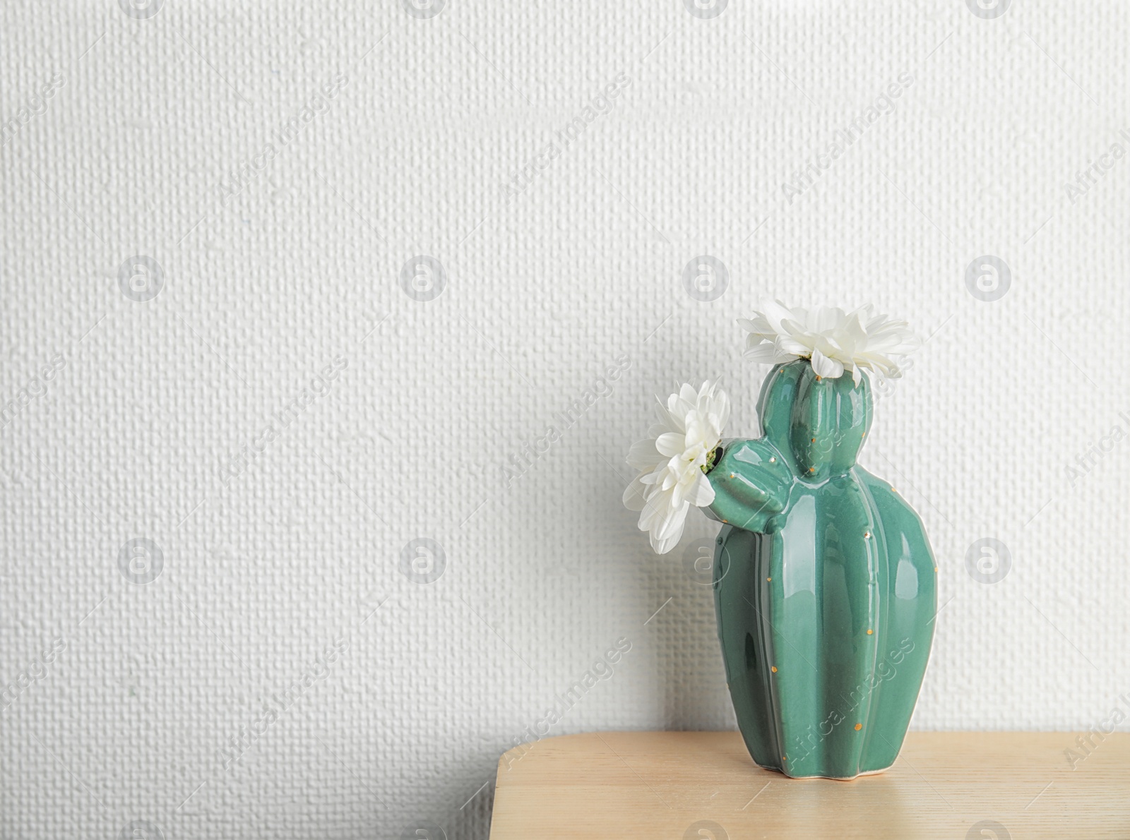 Photo of Trendy cactus shaped vase with flowers on table against light wall. Creative decor