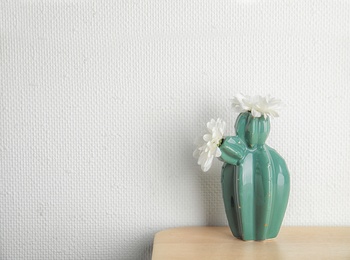 Trendy cactus shaped vase with flowers on table against light wall. Creative decor