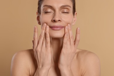 Woman massaging her face on beige background