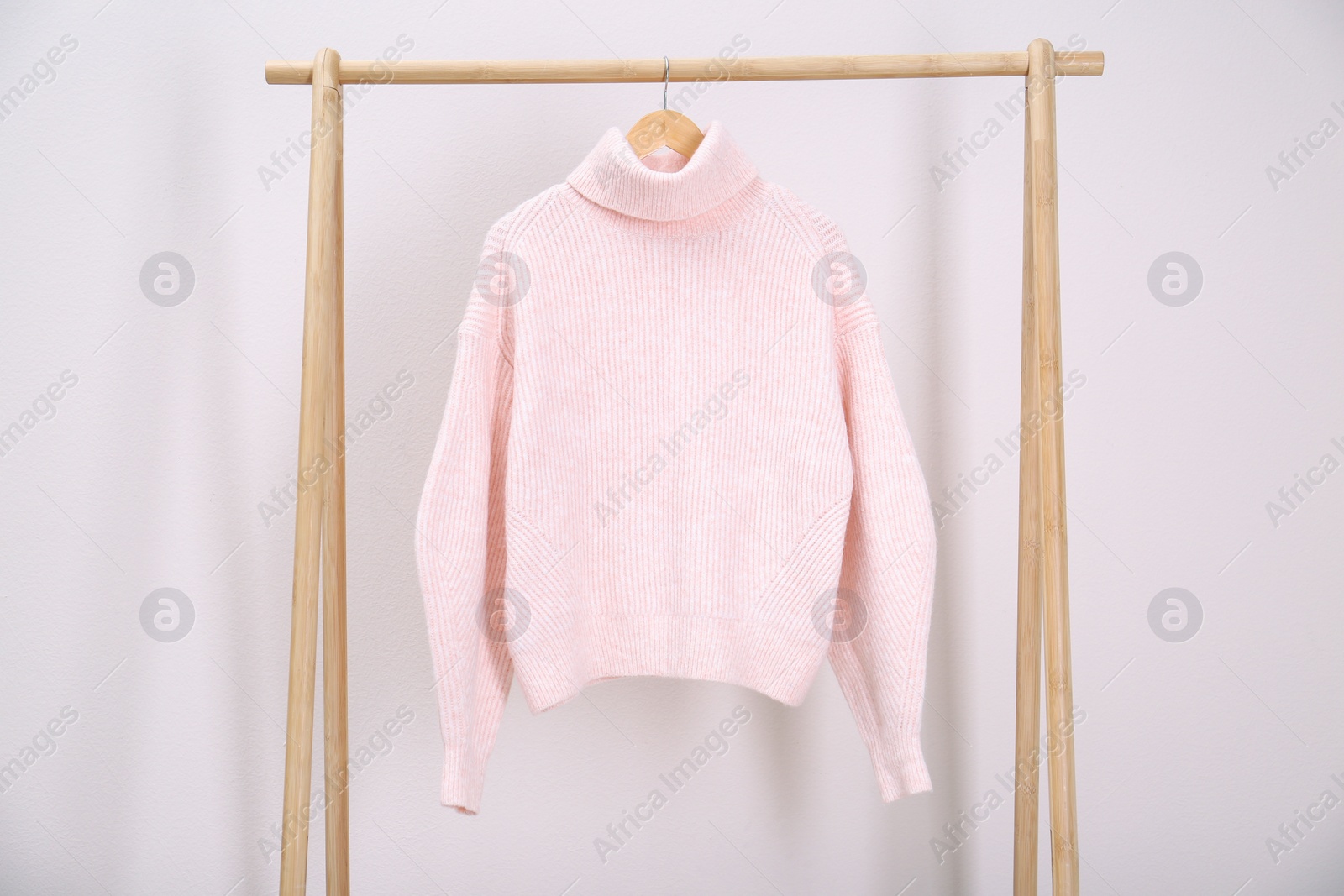 Photo of Stylish knitted sweater hanging on clothing rack near light wall