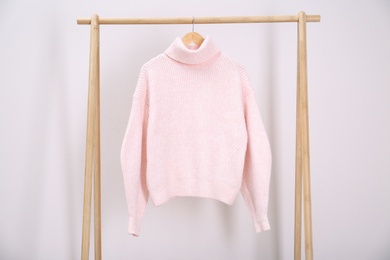 Photo of Stylish knitted sweater hanging on clothing rack near light wall