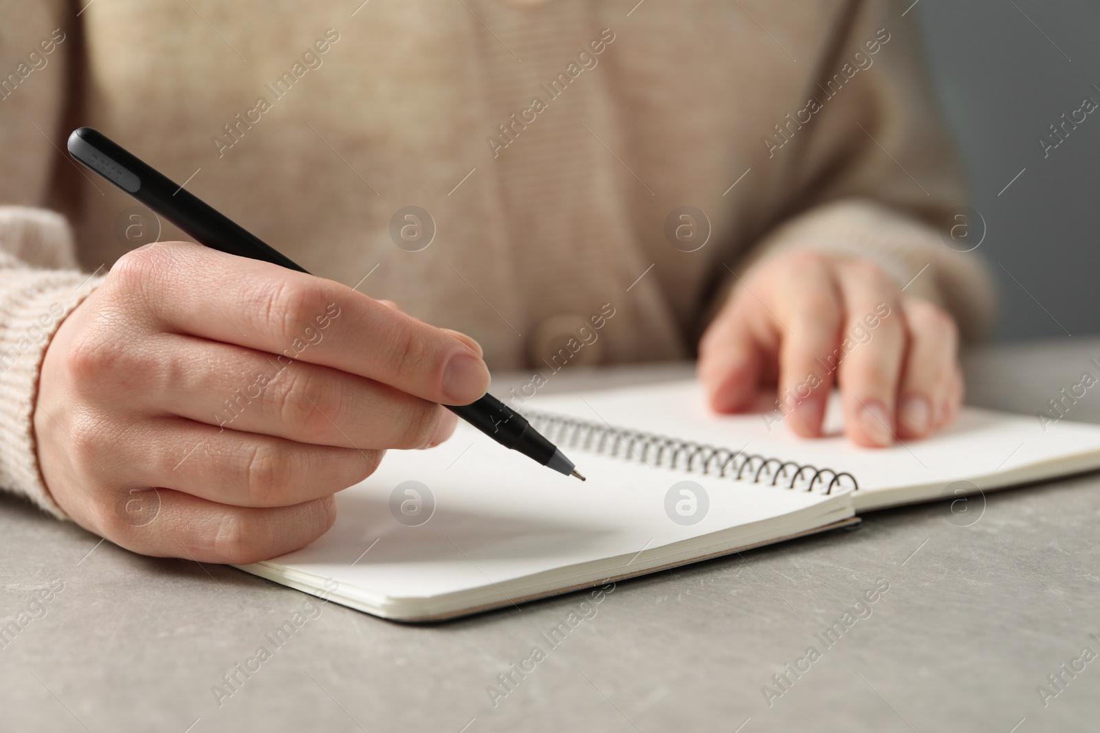 Photo of Woman with pen and notepad at grey table, closeup