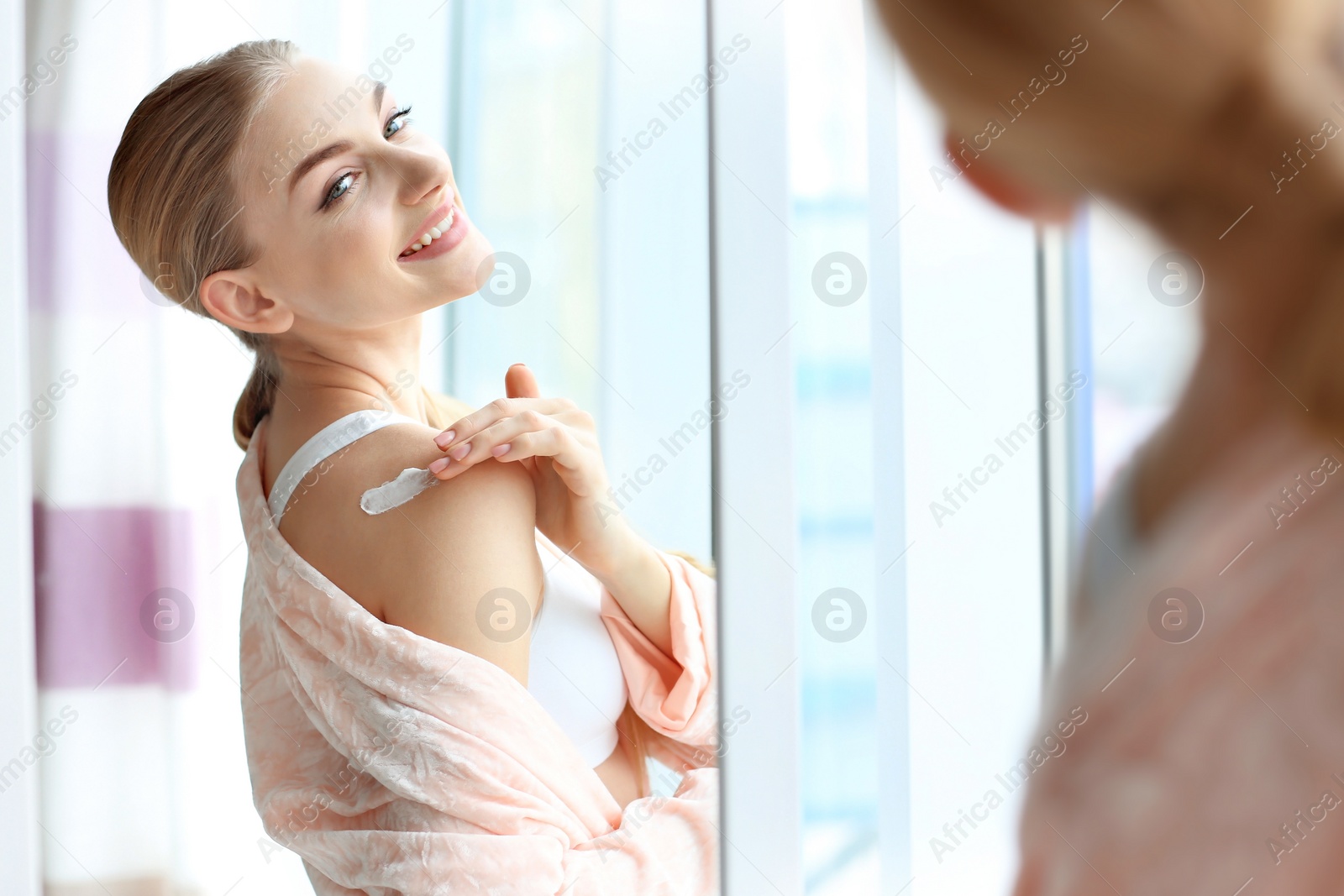 Photo of Young woman applying body cream at home